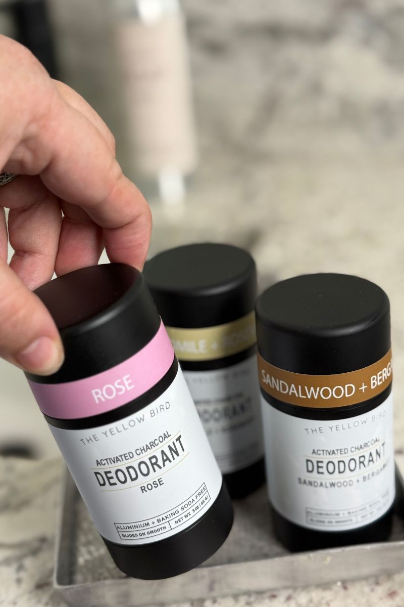Hand choosing a Yellow Bird natural deodorant scent from a tray of charcoal deodorants