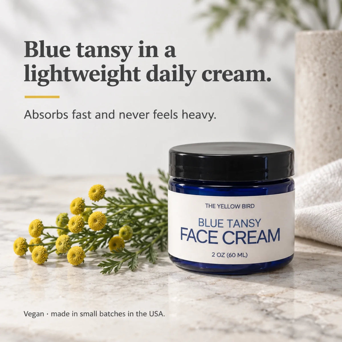 Blue Tansy Face Cream jar on a marble counter beside fresh tansy flowers, a lightweight vegan daily cream made in the USA