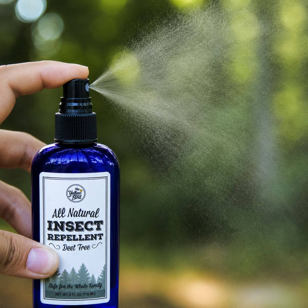 Hand spraying The Yellow Bird natural DEET free insect repellent outdoors with fine mist visible against green trees